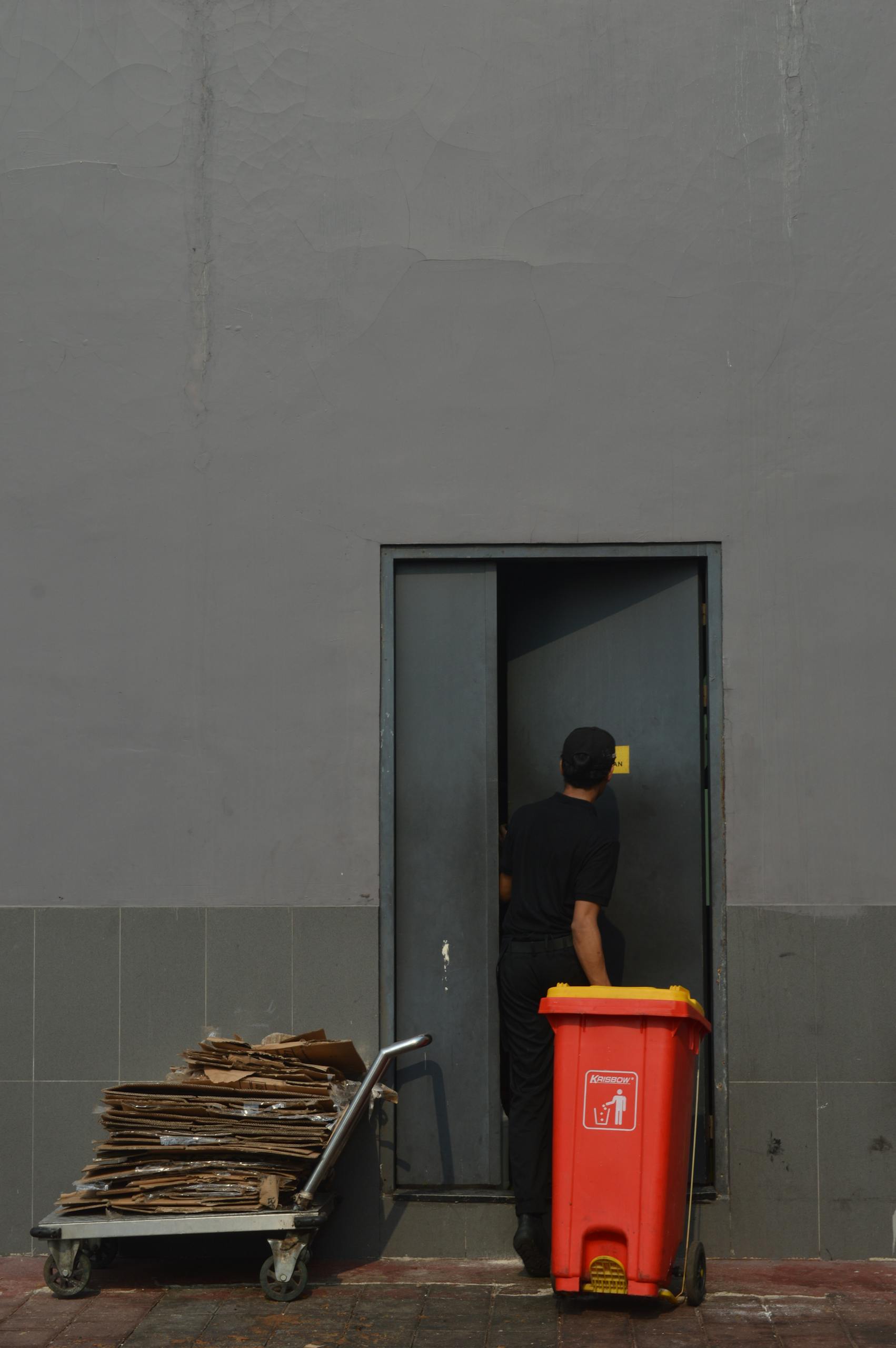 A person disposes of cardboard with a red trash bin, entering an industrial door.